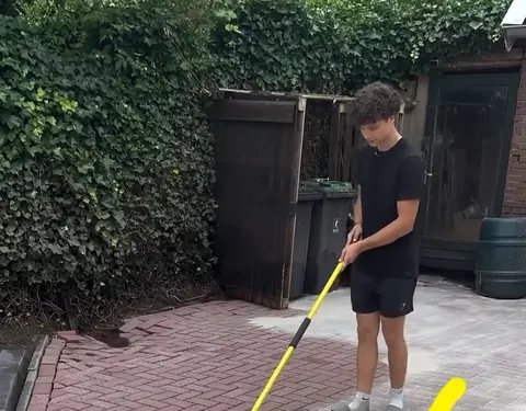 Onkruidremmend voegzand wordt over een gereinigde oprit geveegd